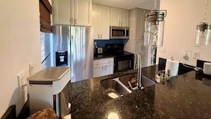 A modern kitchen with stainless steel appliances, a black granite countertop, and white cabinetry.