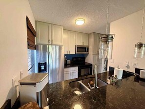 Una cocina moderna con electrodomésticos de acero inoxidable, encimera de granito negro y muebles de cocina blancos.