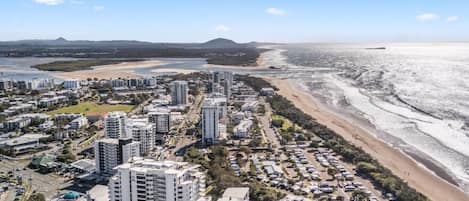 A coastal cityscape with high-rise buildings, a beach, and a river.