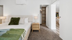 Une chambre moderne avec un lit, des tables de chevet, une armoire et une salle de bain visible à travers une porte ouverte.