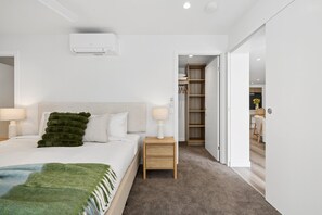 Ein modernes Schlafzimmer mit Bett, Nachttischen, einem Kleiderschrank und einem durch eine offene Tür einsehbaren Badezimmer.