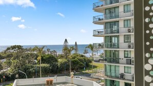 Un immeuble à plusieurs étages doté de balcons donnant sur une plage et l’océan.