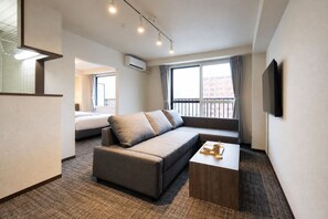 A modern hotel room with a sofa, a bed, a TV, and a balcony with a view. - Residence Hotel Louvre (Chuo-ku, Sapporo)