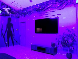 A room with a flat-screen TV mounted on the wall, a dark-colored entertainment unit, and a potted plant. - Once Upon A Vacation Home with Pool + Game Room + Sleeps 9 near DISNEY! (Kissimmee)