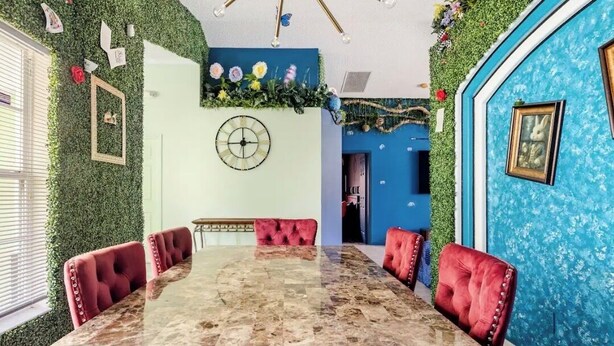 Uma sala de jantar com uma mesa de mármore, cadeiras estofadas vermelhas, um relógio na parede e uma parede azul decorativa.