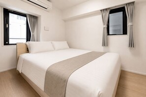 A hotel room with a large bed, a bedside table, an air conditioning unit, and two windows with curtains. - MoriKoYa Hotel · 2BR + Balcony · Senso-ji 5 min (Taito City)