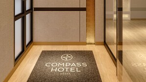 Een hotellobby met een modern design, met een receptiebalie, een glazen scheidingswand en een deurmat met de naam van het hotel.