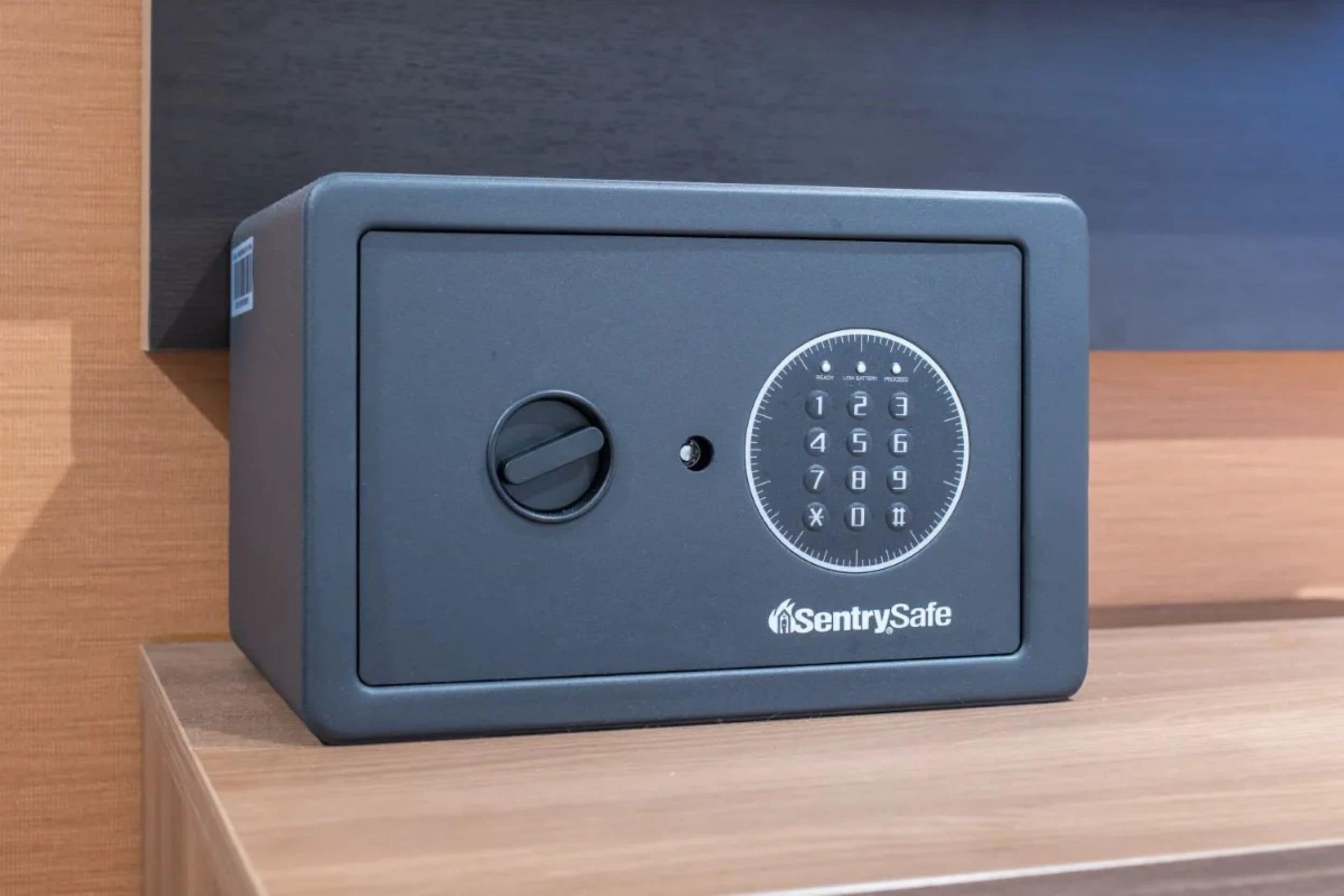 A gray SentrySafe safe with a numeric keypad and a keyhole, placed on a wooden surface.