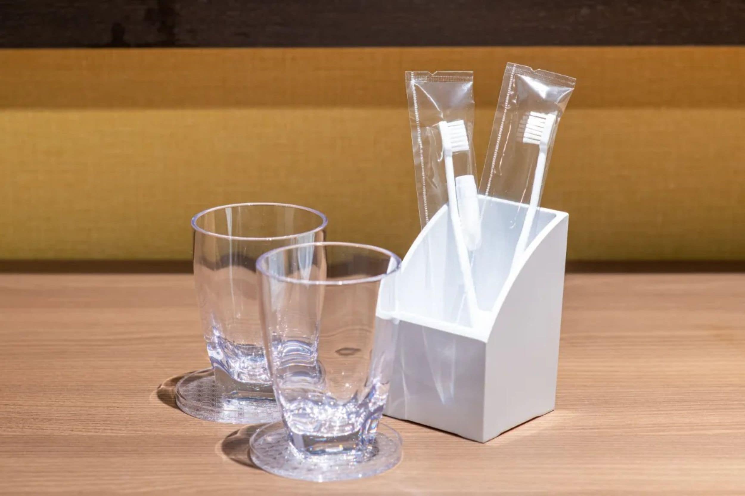 Trois verres transparents et un porte-brosses à dents en plastique blanc, le tout posé sur une surface en bois.