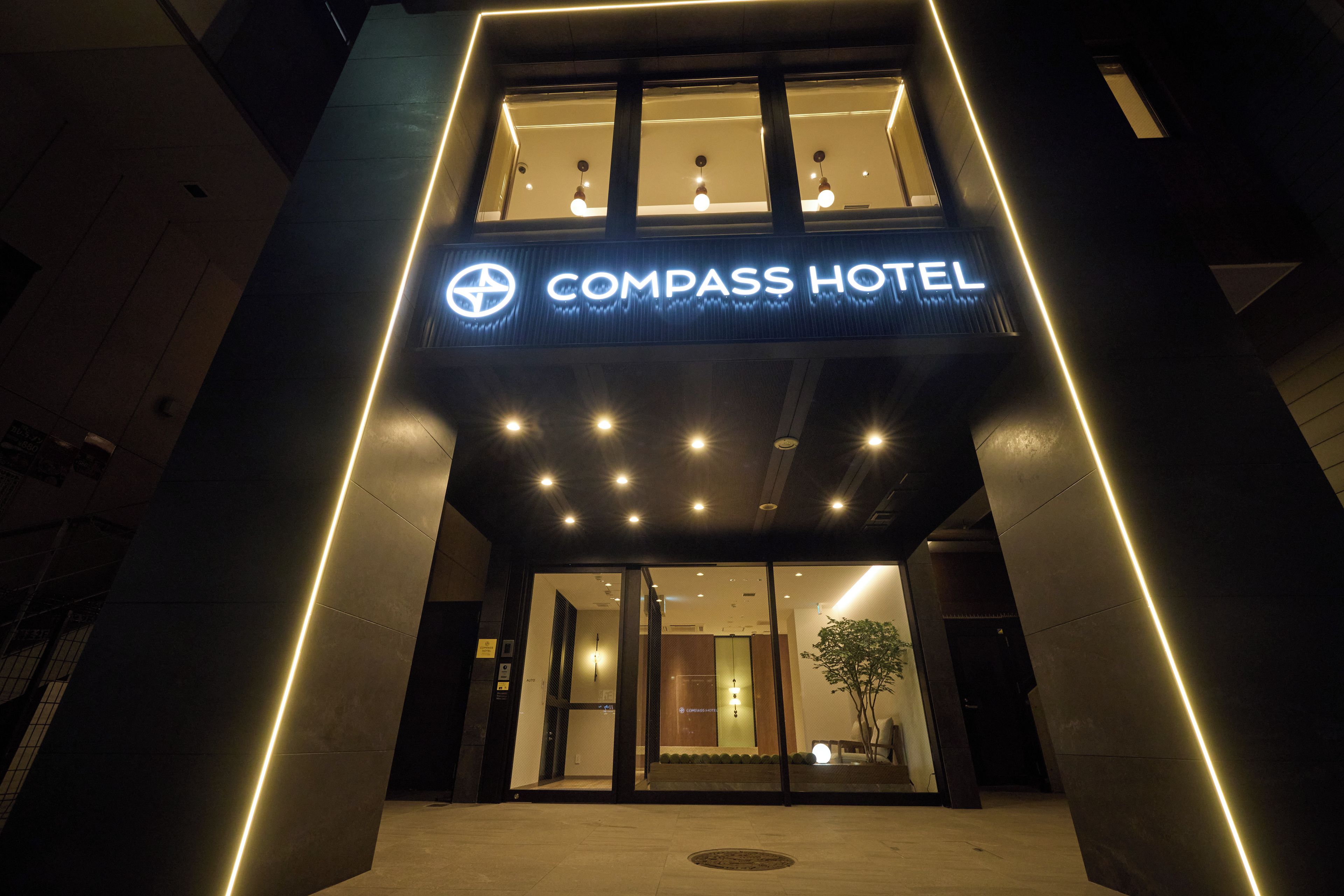 The exterior of Compass Hotel with a modern design, featuring a prominent illuminated sign and a well-lit entrance.