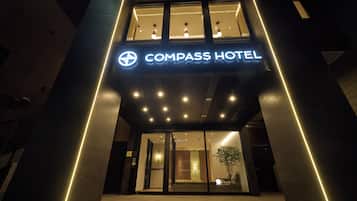 The exterior of Compass Hotel with a modern design, featuring a prominent illuminated sign and a well-lit entrance.
