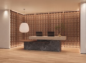 A reception desk with a marble base, two black monitors, and a hanging light fixture.