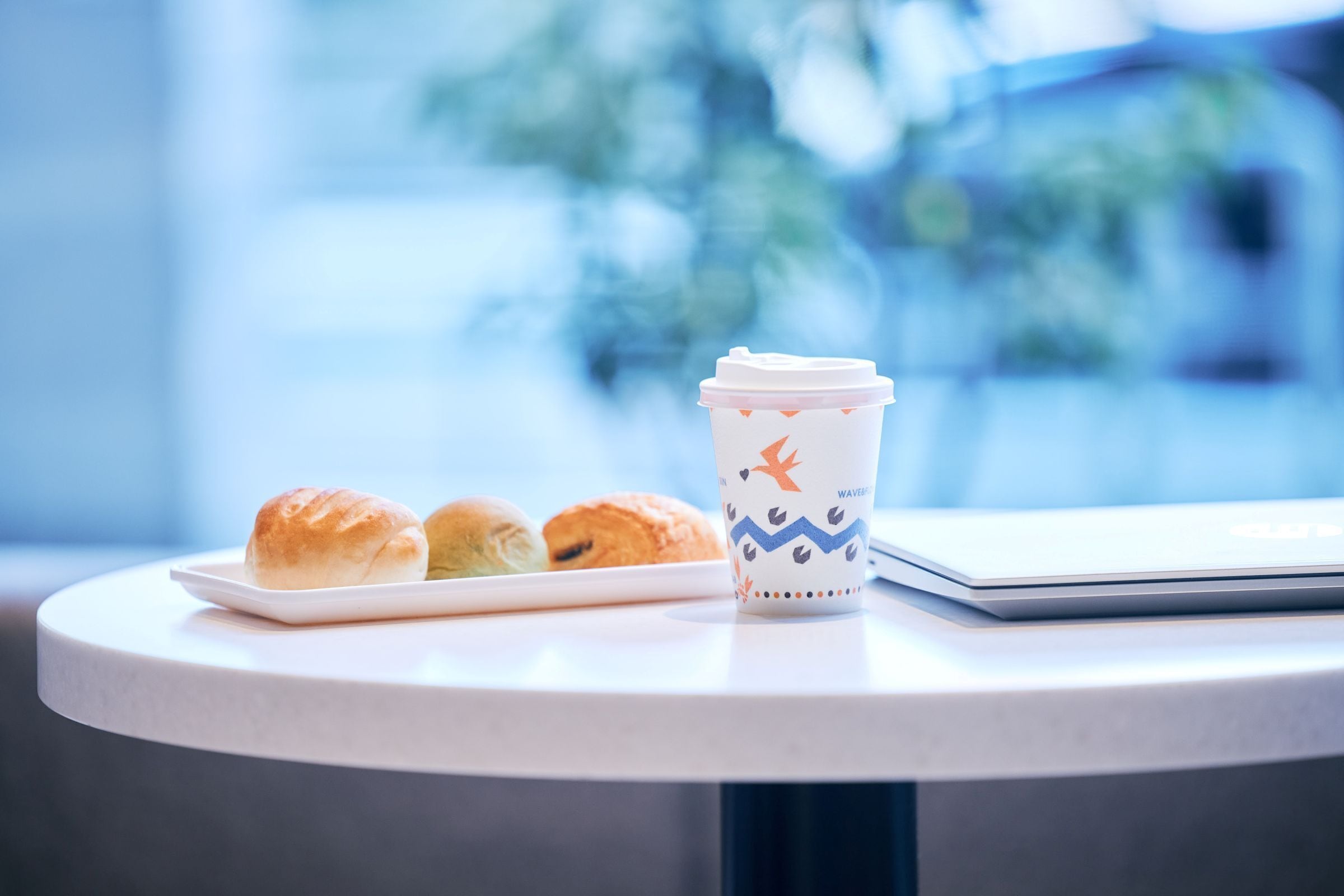 A white table with a white plate of pastries, a coffee cup, and a closed laptop.