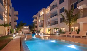 Un hotel moderno con piscina, varios balcones y palmeras.
