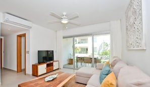 Ein modernes Wohnzimmer mit Flachbildfernseher, Couchtisch aus Holz, Sofa und Deckenventilator.