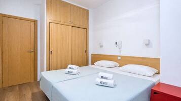 Een hotelkamer met twee bedden, een houten garderobe, een rode bijzettafel en een plafondventilator.