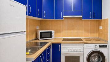 Una cocina con armarios azules, un microondas blanco, una estufa y una lavadora.