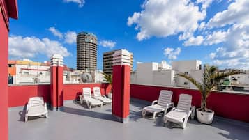 Una terraza en la azotea con sillones blancos, pilares rojos y vistas a edificios de la ciudad.
