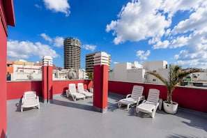 Terraço no telhado com cadeiras de descanso brancas, pilares vermelhos e vista para edifícios da cidade.
