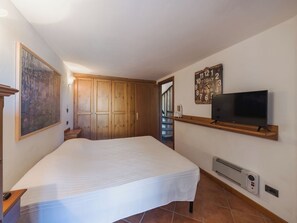 Ein Schlafzimmer mit einem Bett, einem Holzschrank, einem Gemälde, einer Uhr und einem Fernseher.