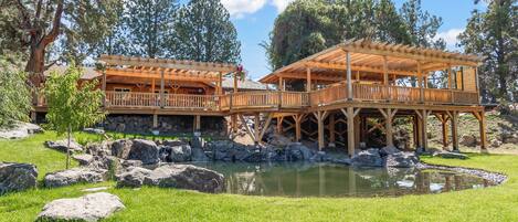 A wooden gazebo with a stone foundation, surrounded by a pond and large rocks.