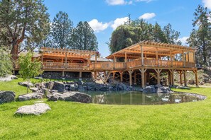 A wooden gazebo with a stone foundation, surrounded by a pond and large rocks.
