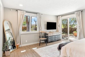 A bedroom with a large mirror, a TV, a wooden dresser, and a bed.