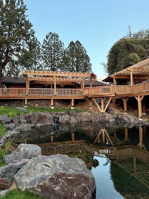 Una terraza de madera con un sendero de piedra que lleva a un estanque, rodeado de árboles.