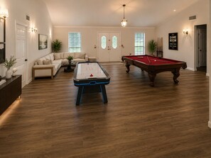 A spacious room with a pool table, a foosball table, a sofa, and a billiards table.