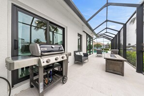 Een moderne buitenpatio met een Weber-grill, tuinmeubilair en grote ramen met uitzicht op de omgeving.