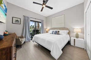 Ein Schlafzimmer mit einem Bett, einem Schreibtisch, einem Stuhl, einem Deckenventilator, einem Nachttisch und einem Fenster mit Jalousien.