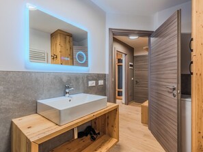 Un baño moderno con un espejo grande, un lavabo blanco, muebles de madera y un banco de madera.