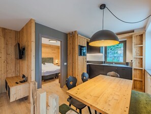 Habitación moderna y compacta con detalles de madera, una mesa de comedor, zona de cocina y una cama.