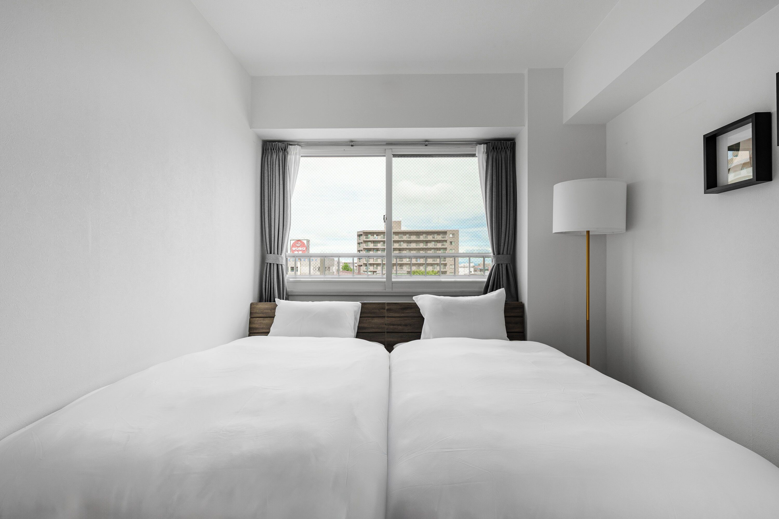 A hotel room with a large bed, a window with curtains, a bedside lamp, and a view of buildings outside.