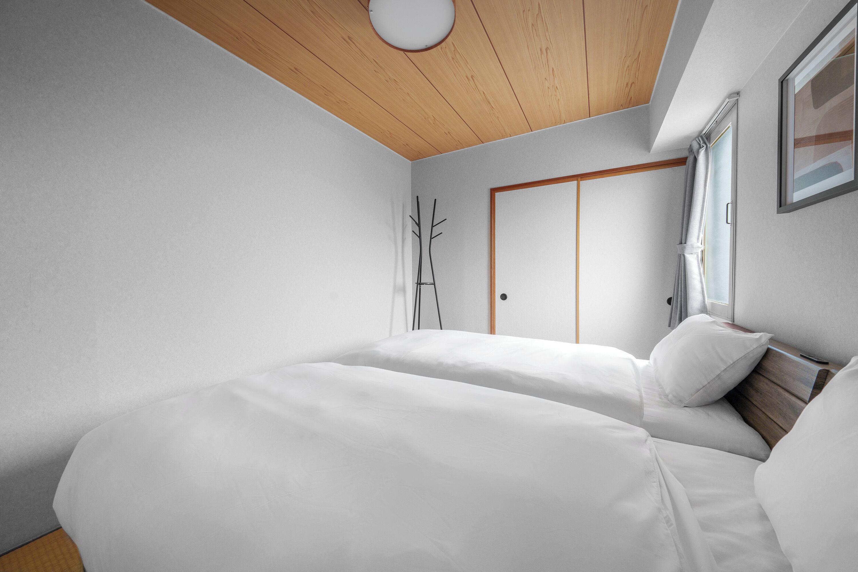 A bedroom with two beds, a wooden ceiling, a wardrobe, and a window with curtains.