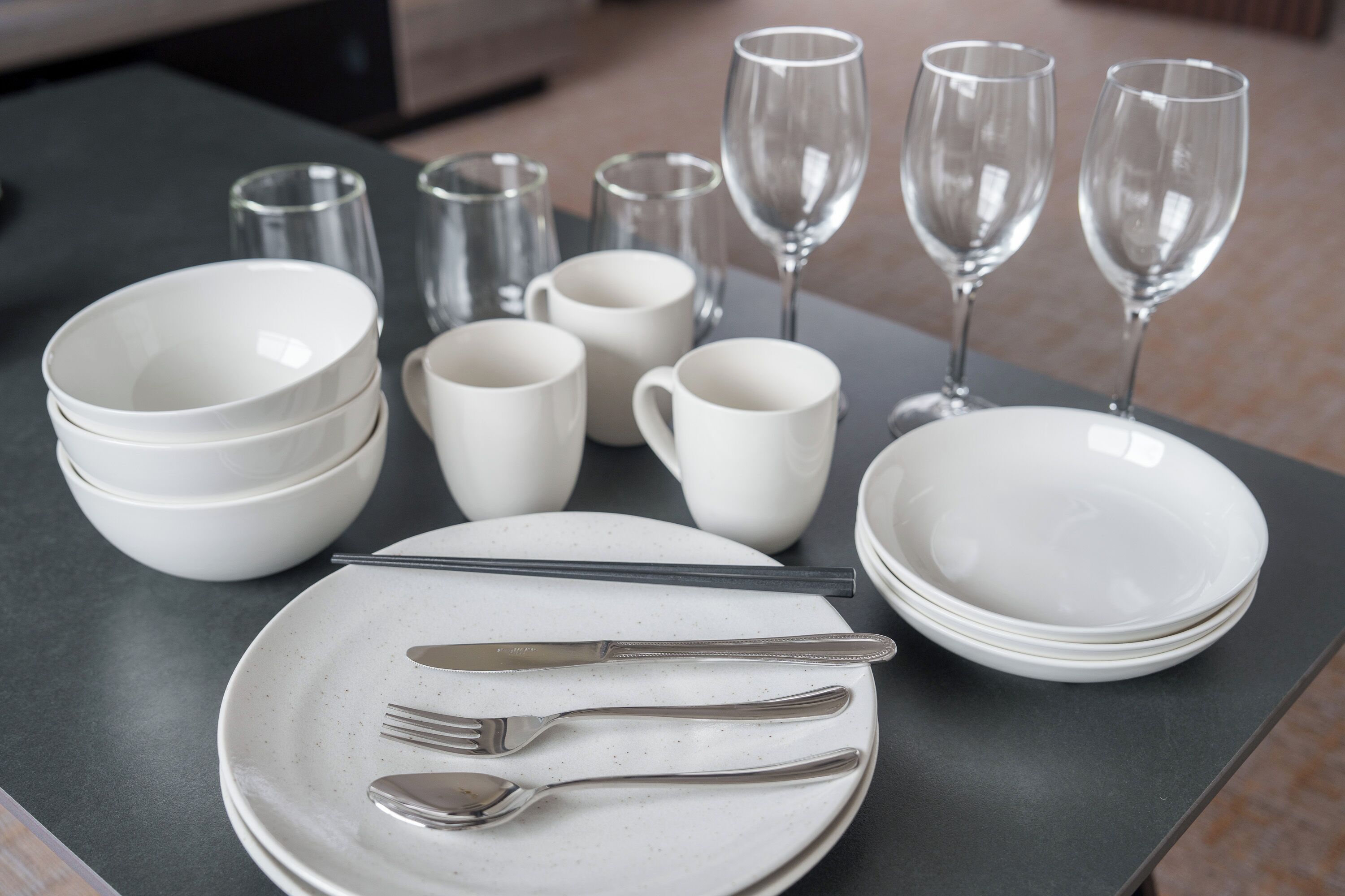 A table set with white dinnerware, including plates, bowls, and cups, along with cutlery and wine glasses.