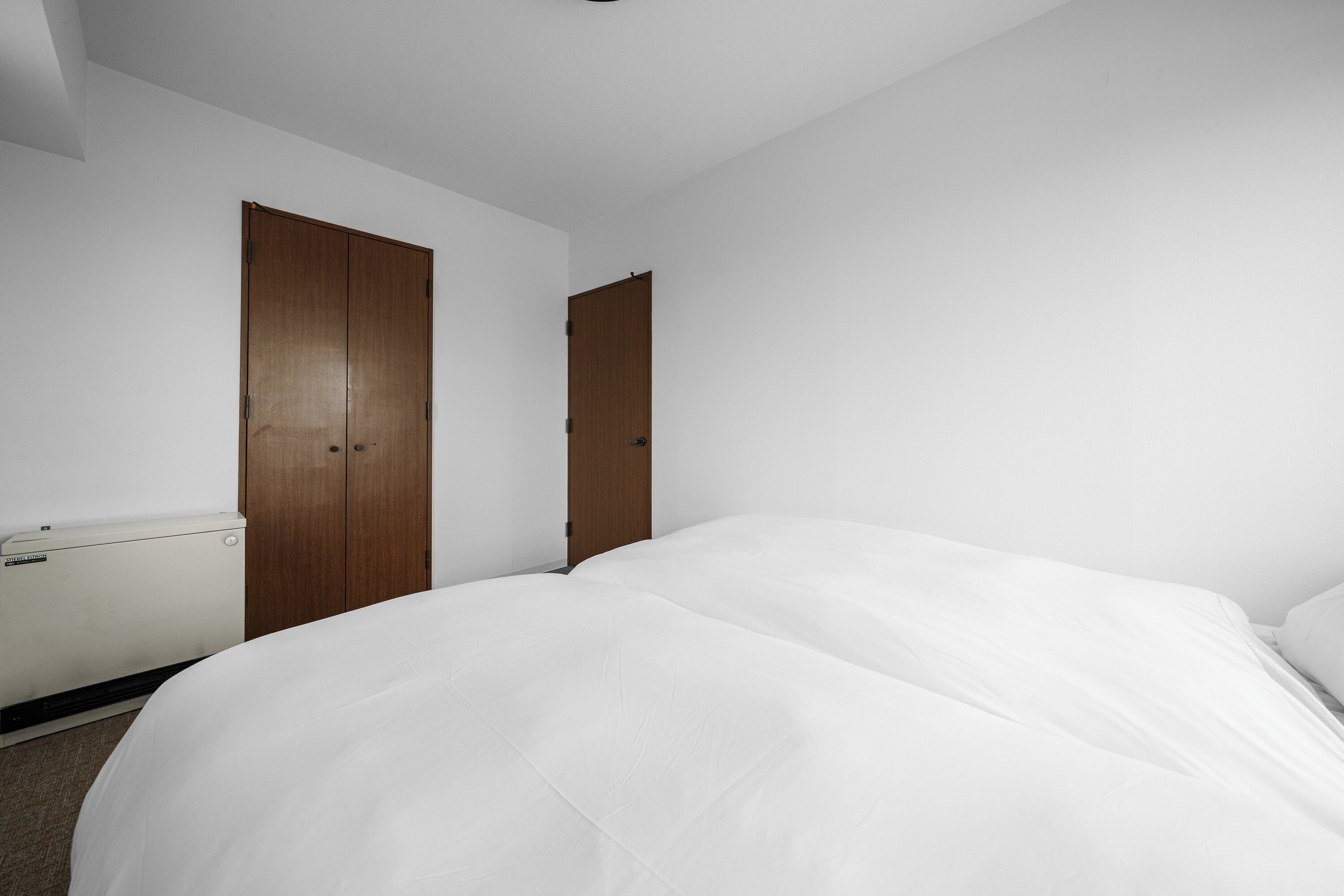 Een kamer met twee houten kasten, een bed met wit beddengoed en een radiator aan de muur.