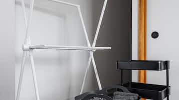 A room with a white metal folding chair, a black storage cart, and a black perforated basket on a carpeted floor.