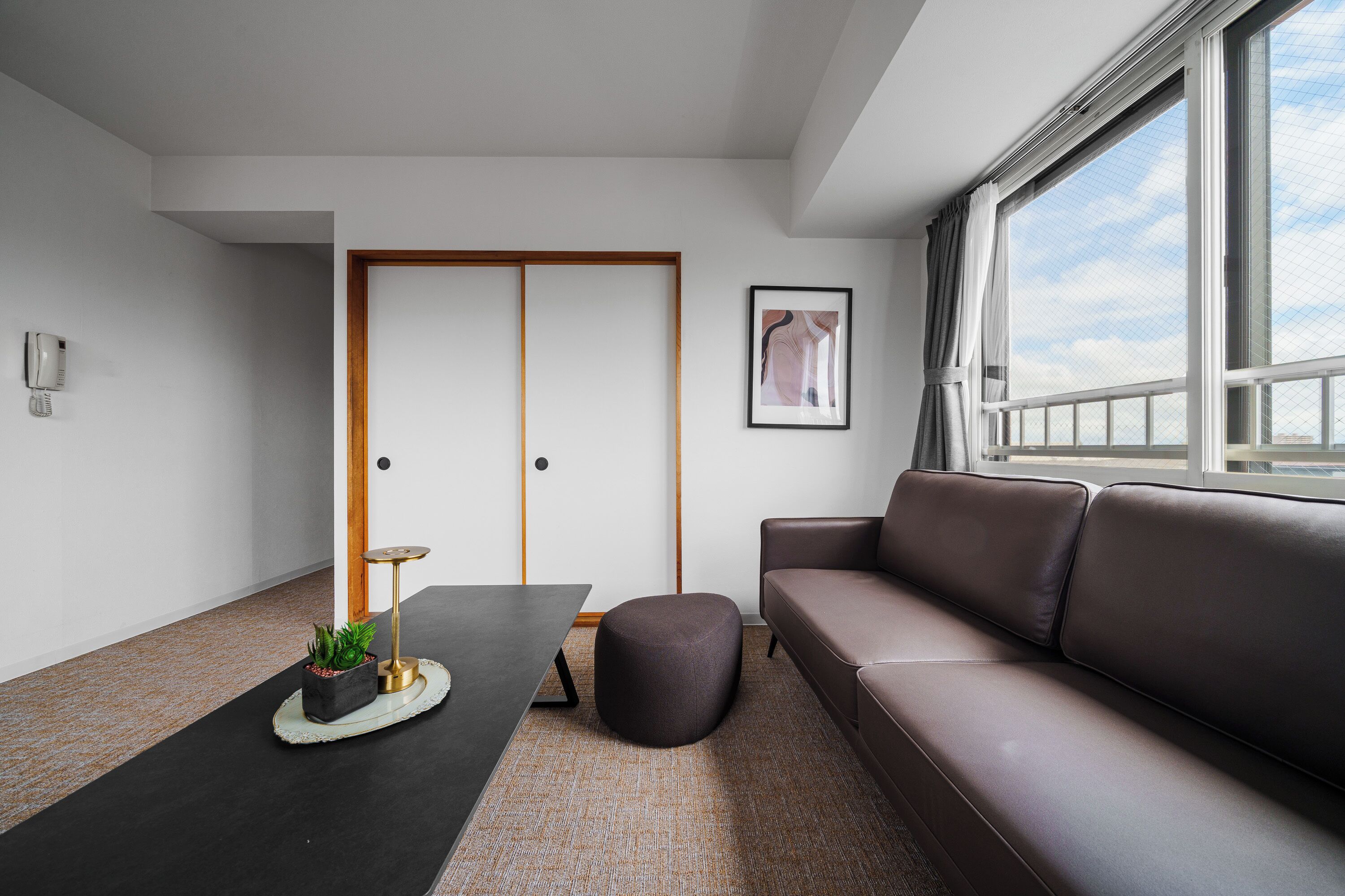 A modern living room with a sofa, a coffee table, a small round ottoman, a framed artwork, and a telephone on the wall.