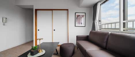 Una sala de estar moderna con un sofá, una mesa de centro, un otoman pequeño y redondo, una obra de arte enmarcada y un teléfono en la pared.
