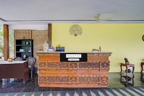 A reception area with a wooden counter labeled 'PALETTE,' a ceiling fan, a wall clock, and a decorative tree.