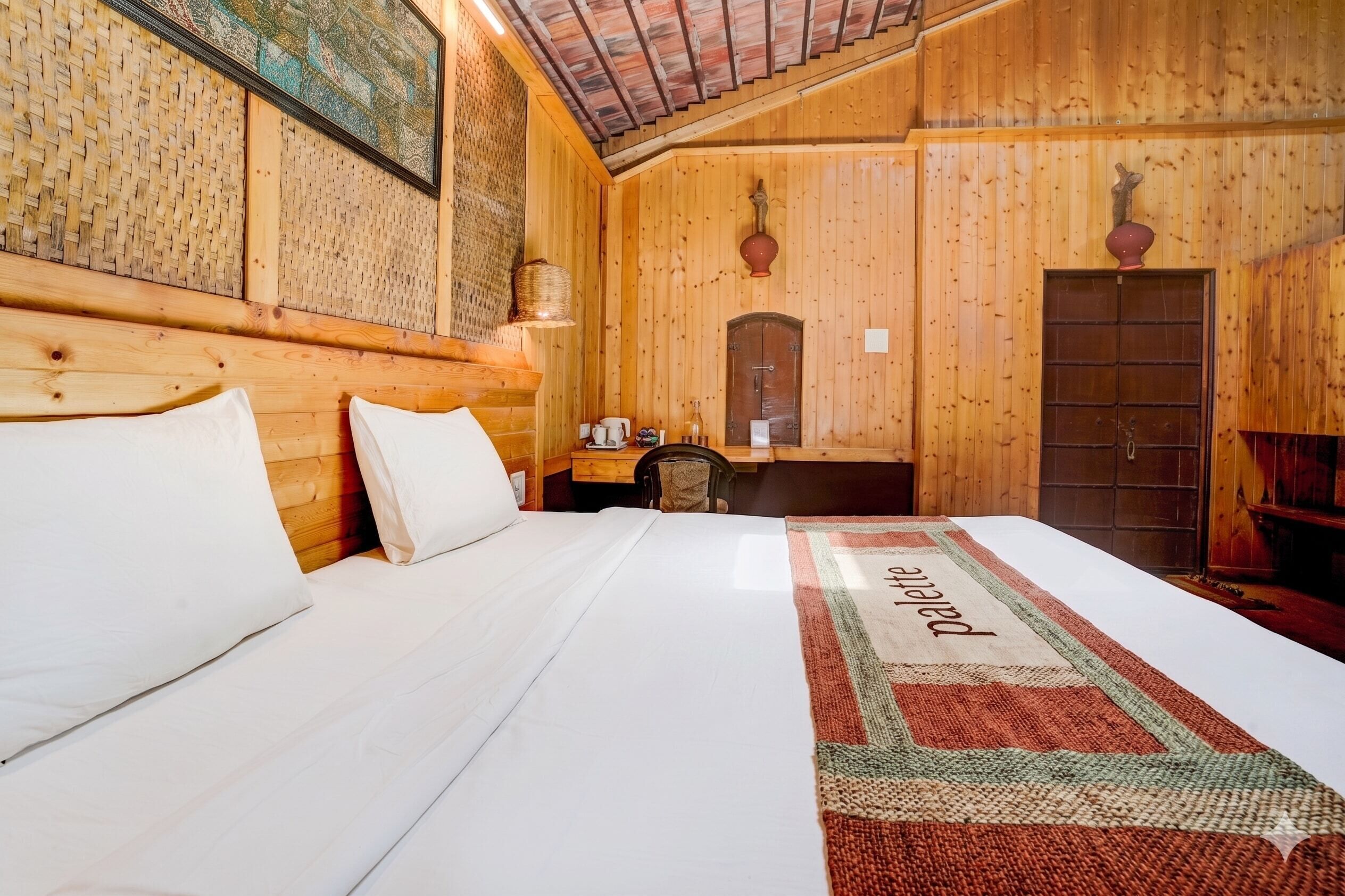 A wooden room with a bed, a small table with a lamp, and a door.