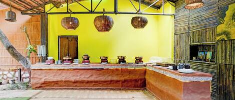 A room with a yellow wall, a wooden bench with dishes, and hanging wicker lamps.