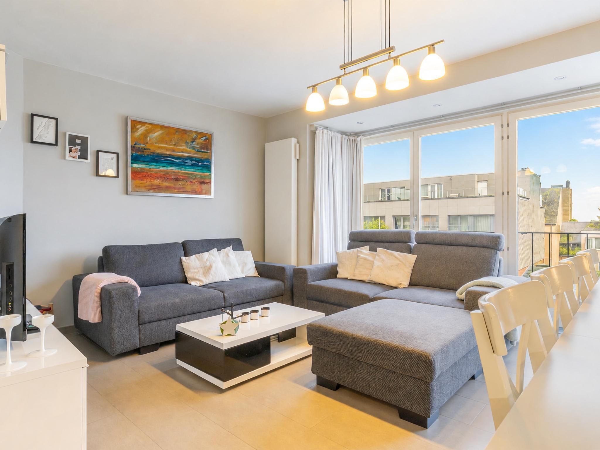 A modern living room with a grey sofa set, a white coffee table, and a large window with curtains.