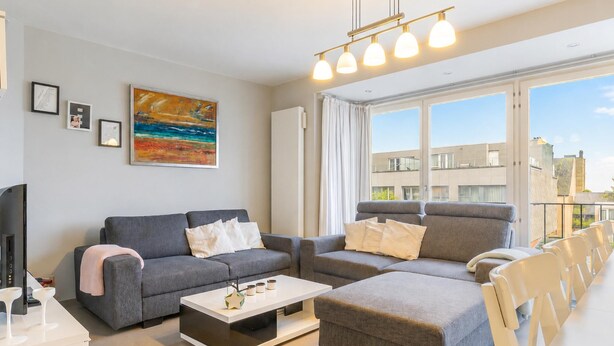 A modern living room with a grey sofa set, a white coffee table, and a large window with curtains. - Spacious 2-Bedroom Apartment Near the Sea (Blankenberge)
