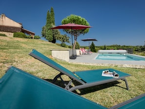 A poolside area with lounge chairs, a pool, and a red umbrella. - Spacious holidayhome with a pool and a wide view (Sauveterre la Lemance)