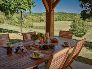 Ein Holz-Esstisch im Freien, gedeckt für eine Mahlzeit, mit Stühlen und einer umliegenden Naturlandschaft.