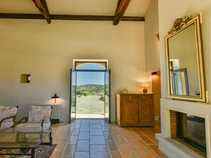 A room with a fireplace, a mirror, a wooden cabinet, a sofa, and a view through a glass door. - Spacious holidayhome with a pool and a wide view (Sauveterre la Lemance)