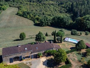 A stone building with a tiled roof, a swimming pool, and a surrounding grassy area with trees. - Spacious holidayhome with a pool and a wide view (Sauveterre la Lemance)