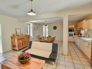 A modern kitchen with wooden cabinets, a dining area with a sofa, and a table with a flower centerpiece. - Spacious holidayhome with a pool and a wide view (Sauveterre la Lemance)